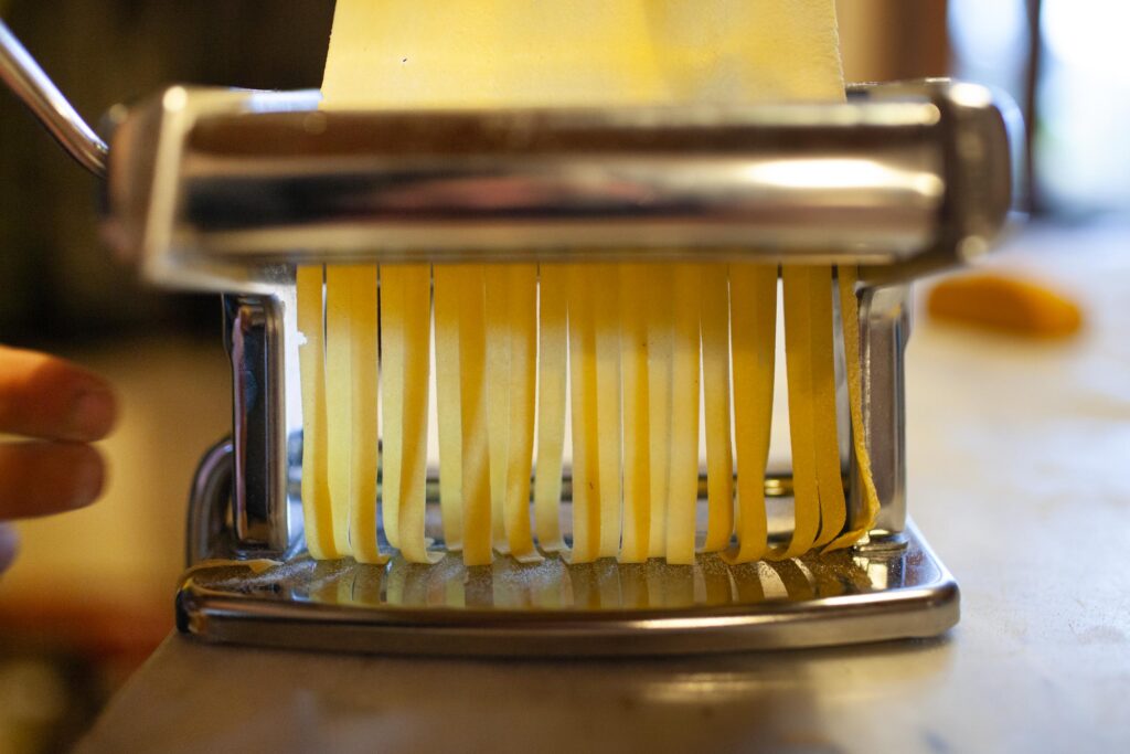 Close-up of fresh tagliatelle being cut from a pasta sheet